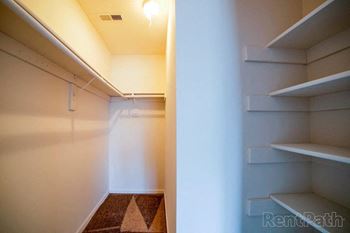 a walk in closet with white shelves and a white wall